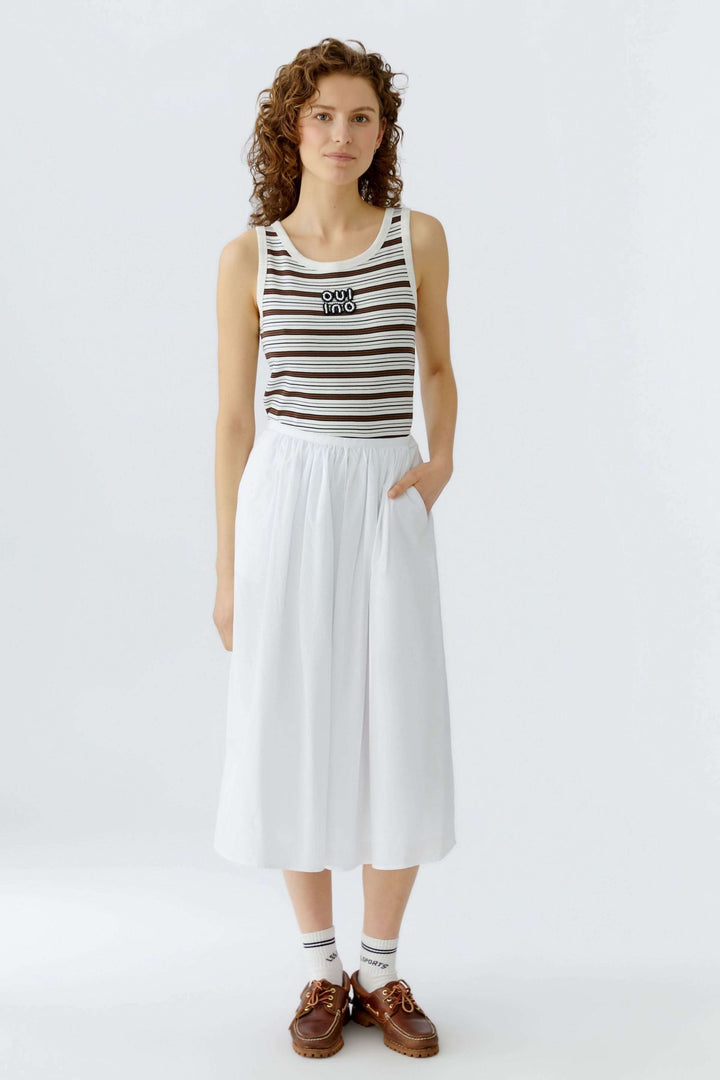 Femme portant une camisole à rayures avec encolure arrondie, bretelles larges et détail brodé, idéale pour un look estival moderne.