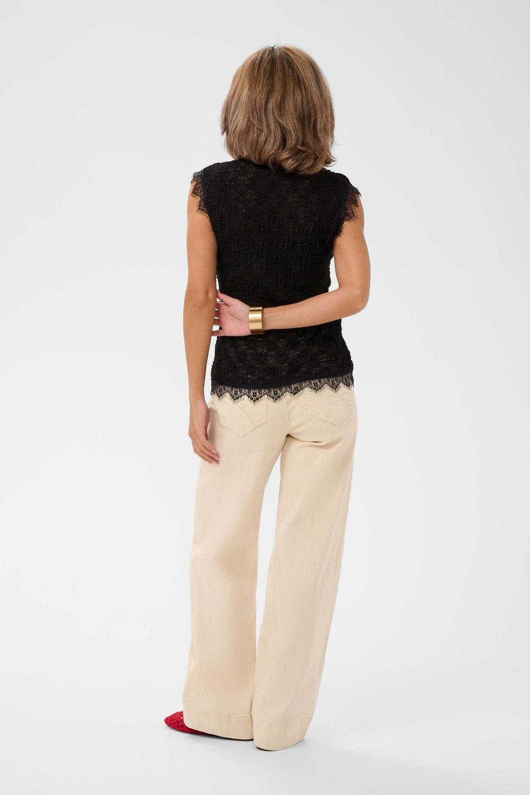 Femme portant une camisole sans manches en dentelle noire avec pantalon beige, vue de dos.