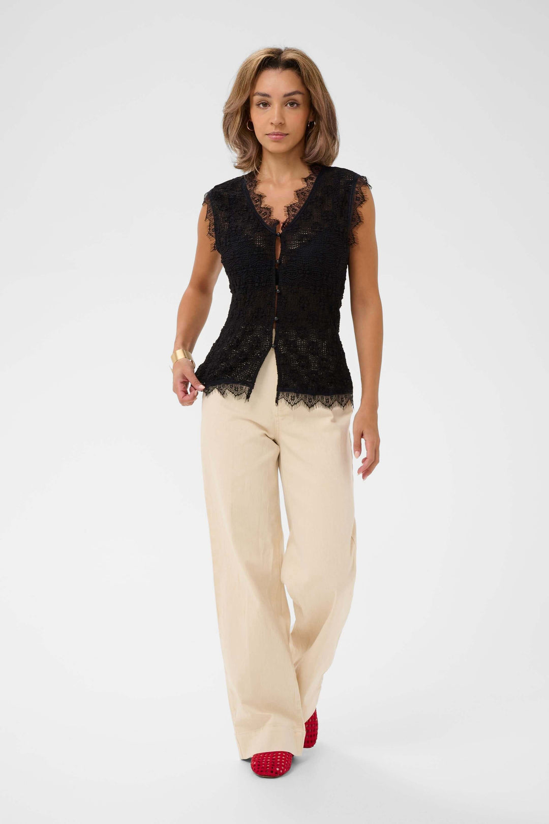 Femme portant une camisole sans manches en dentelle, élégante et féminine, avec des bordures festonnées et fermeture boutonnée.