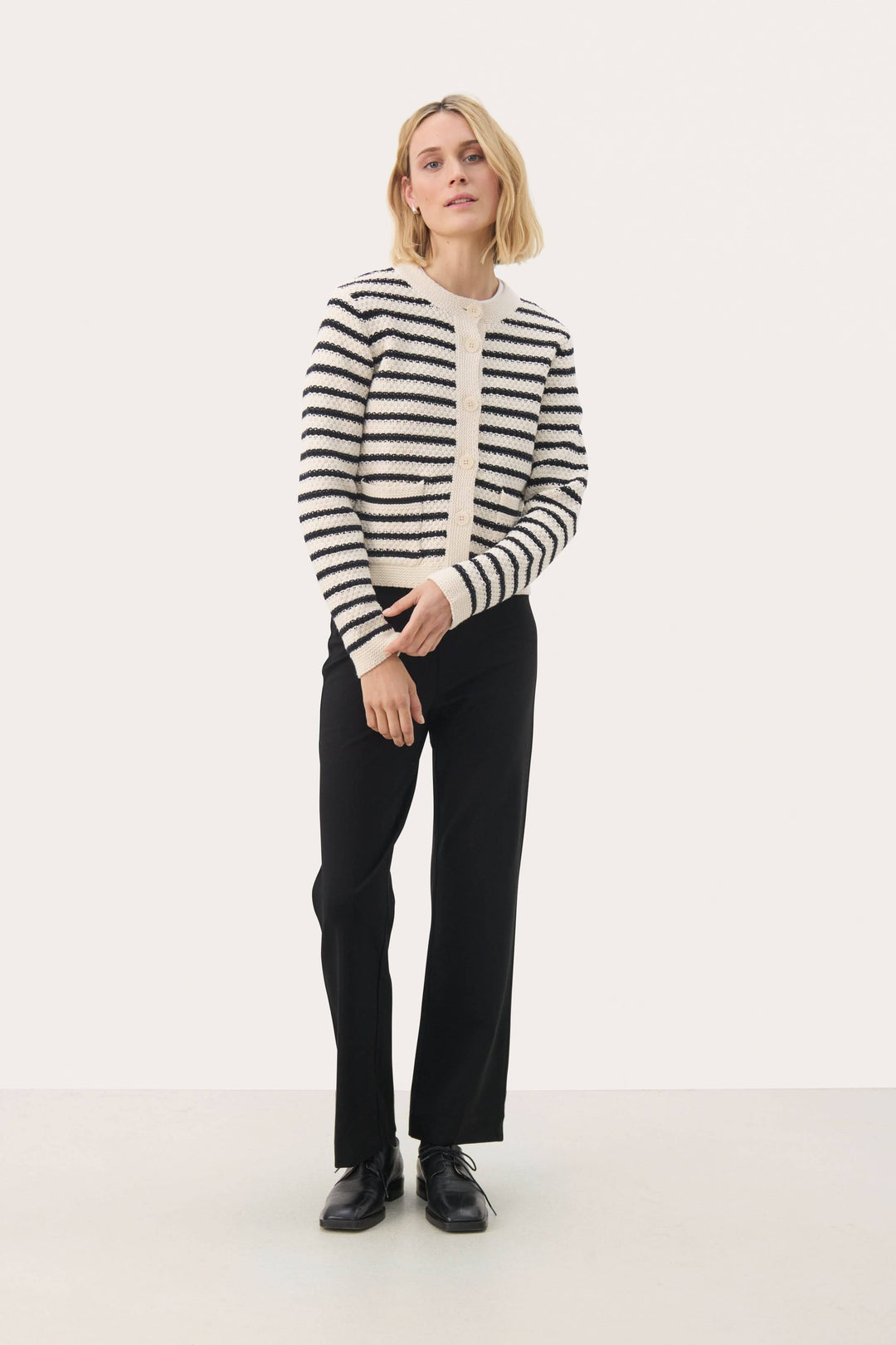Femme portant un cardigan Elmie à rayures horizontales avec un pantalon noir, offrant une élégance moderne et décontractée.