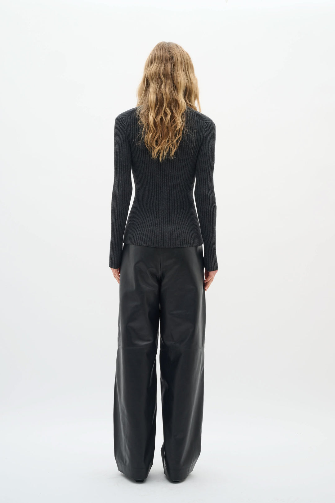 Woman wearing a fitted black ribbed cardigan with a stylish back view, paired with loose leather pants.