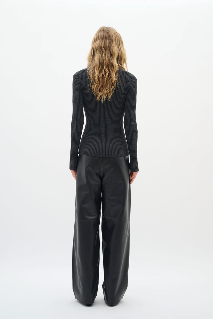 Woman wearing a fitted black ribbed cardigan with a stylish back view, paired with loose leather pants.