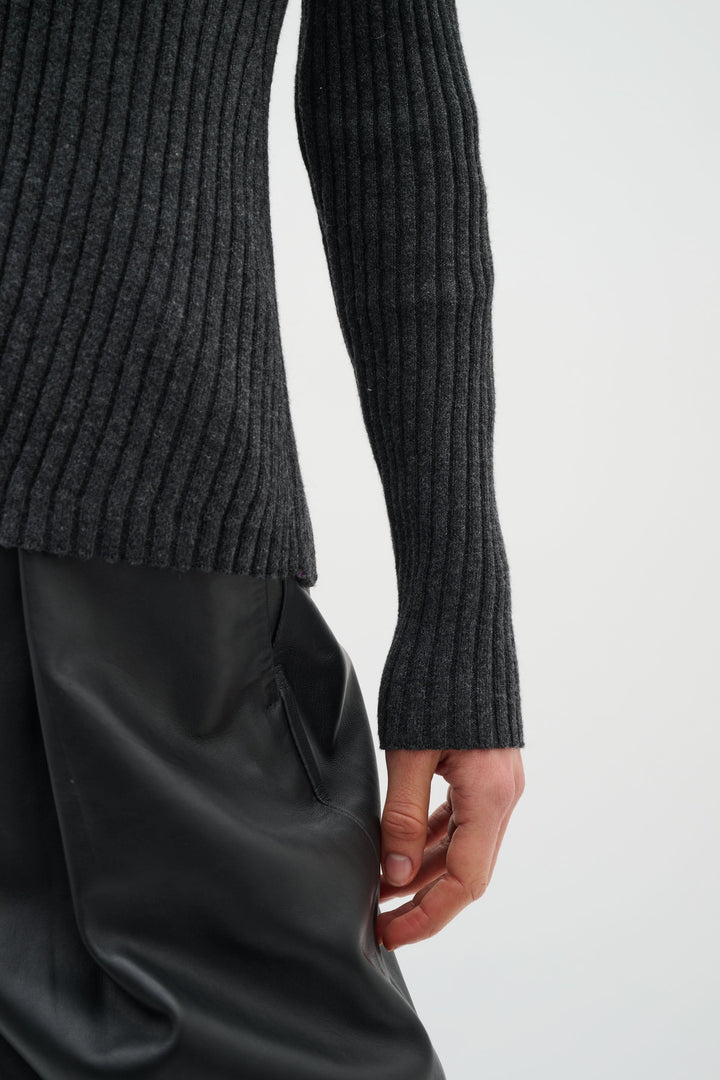 Manche d'un cardigan à côtes fines en gris, porté avec un pantalon noir, mettant en avant l'élégance et le confort.