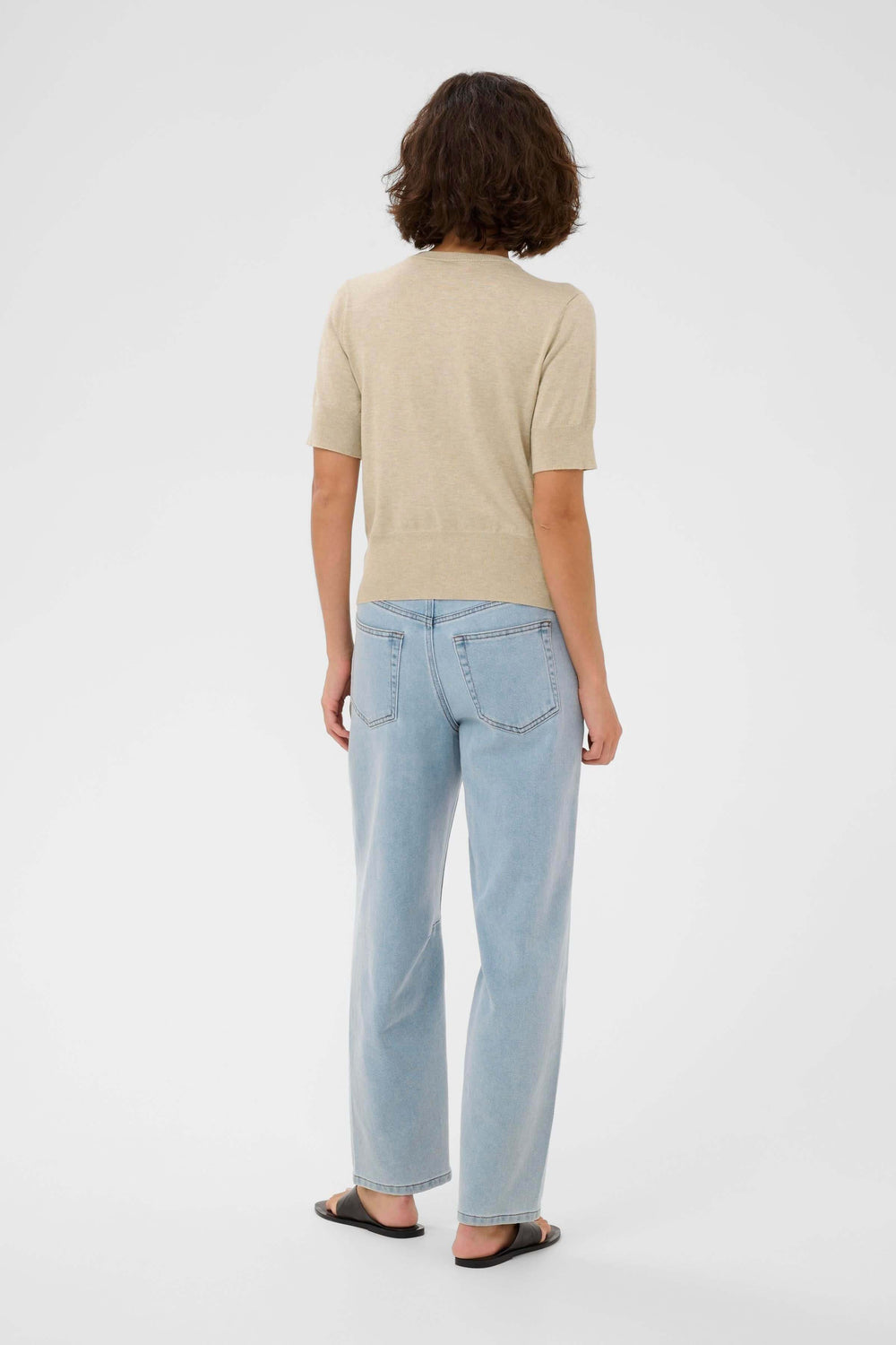 Vue arrière d'un modèle portant le Cardigan Lizza à manches courtes et une paire de jeans casual, style épuré et féminin.