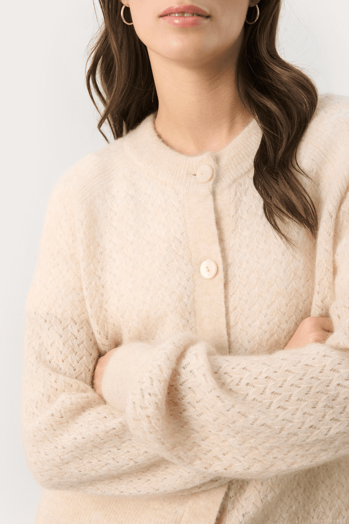 Cardigan Thora en tricot fin beige avec encolure ronde et fermeture à boutons, idéal pour un look décontracté chic.