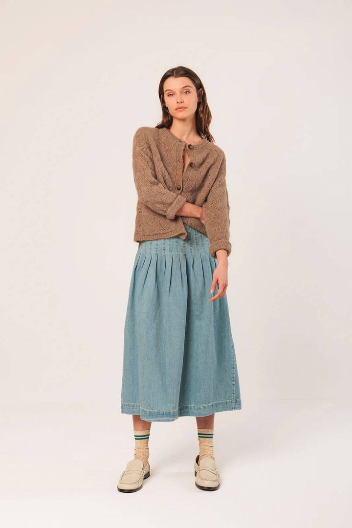 Modèle portant un cardigan crochet beige avec une jupe denim bleu, style décontracté et chic, idéal pour les journées fraîches.