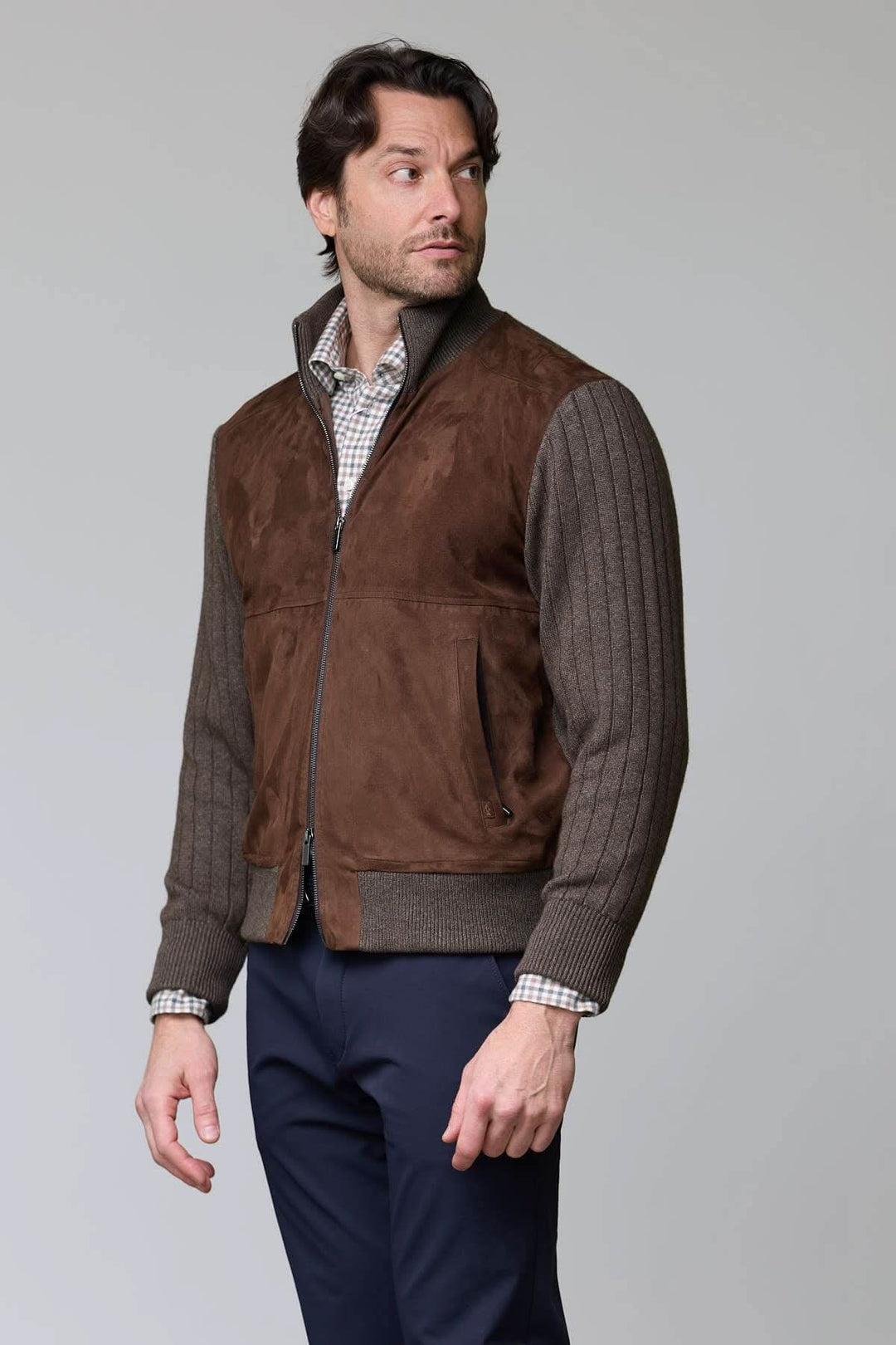 Homme portant un cardigan à empiècements en suédine avec fermeture éclair et col montant, élégant et décontracté, sur fond neutre.