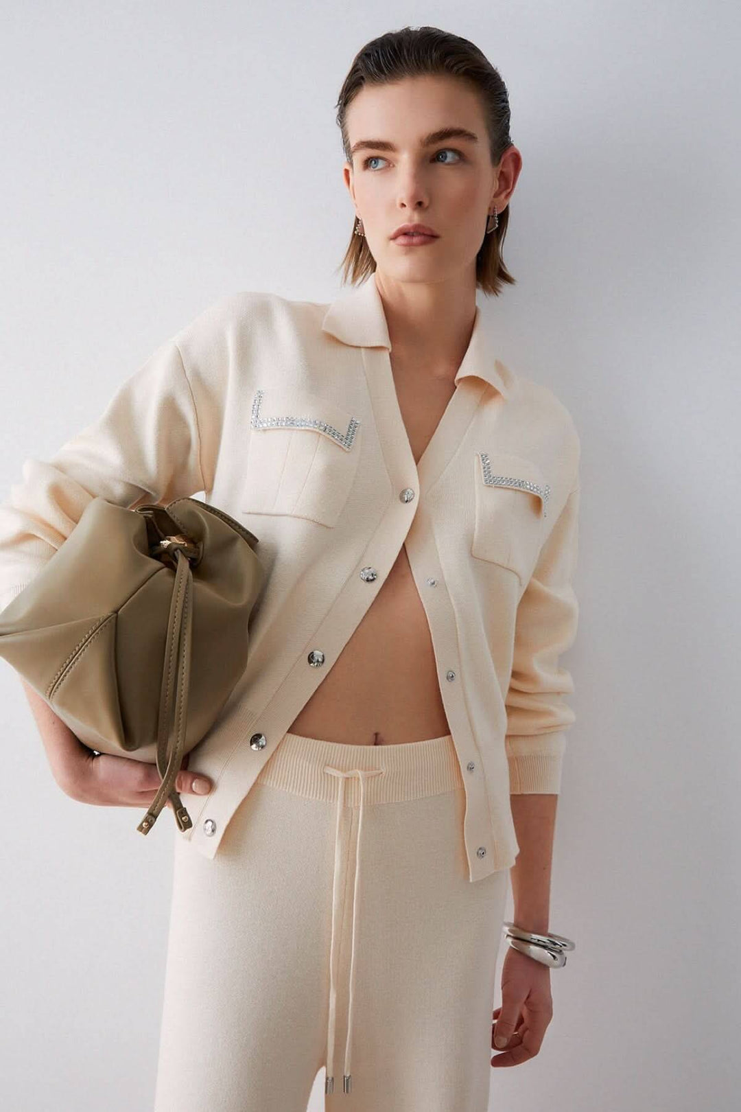 Femme portant un cardigan en maille avec poches décoratives, col chemisier et fermeture boutonnée, combiné avec un pantalon décontracté.
