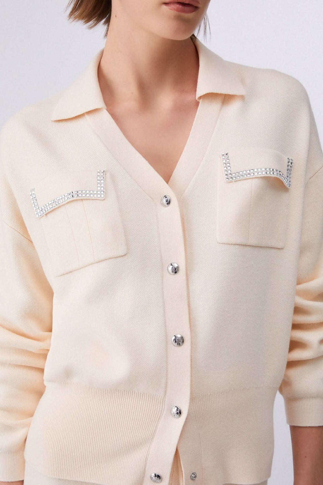 Cardigan en maille avec poches décoratives et col chemisier, détail chic sur les poches pour un look élégant et moderne.