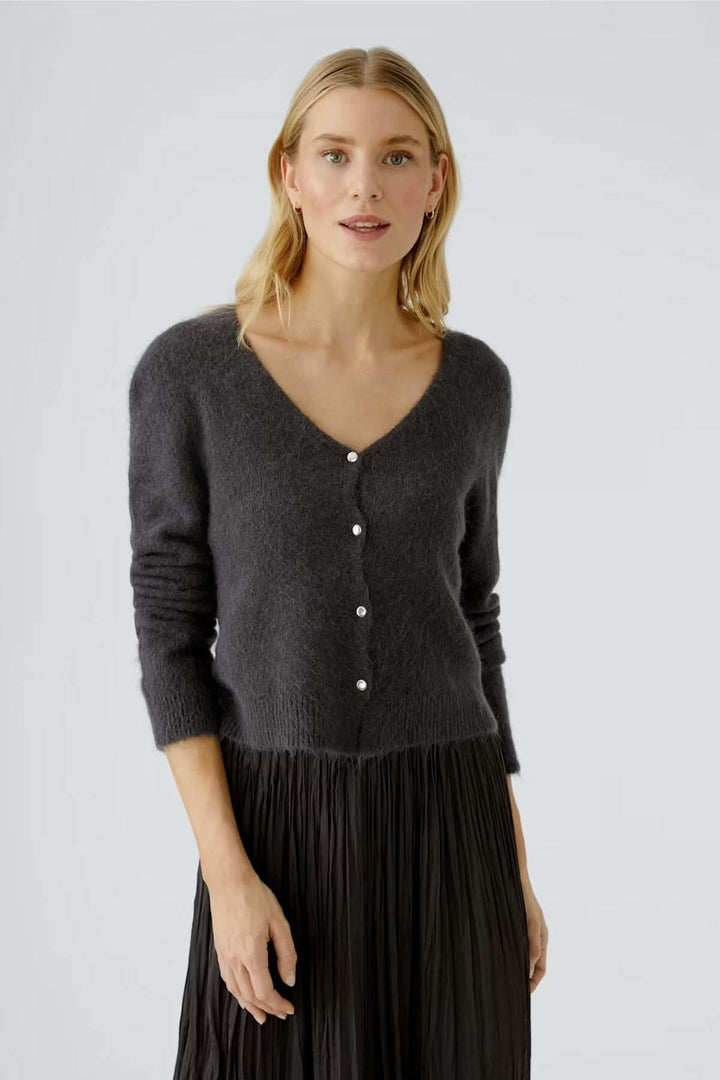 Femme portant un cardigan à encolure en V avec boutons contrastés, coupe courte féminine et maille duveteuse, robe noire plissée.