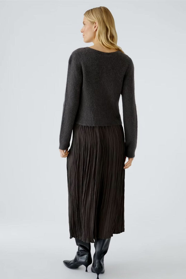 Femme portant un cardigan à encolure en V et une jupe plissée marron, vue de dos. Style chic et moderne.