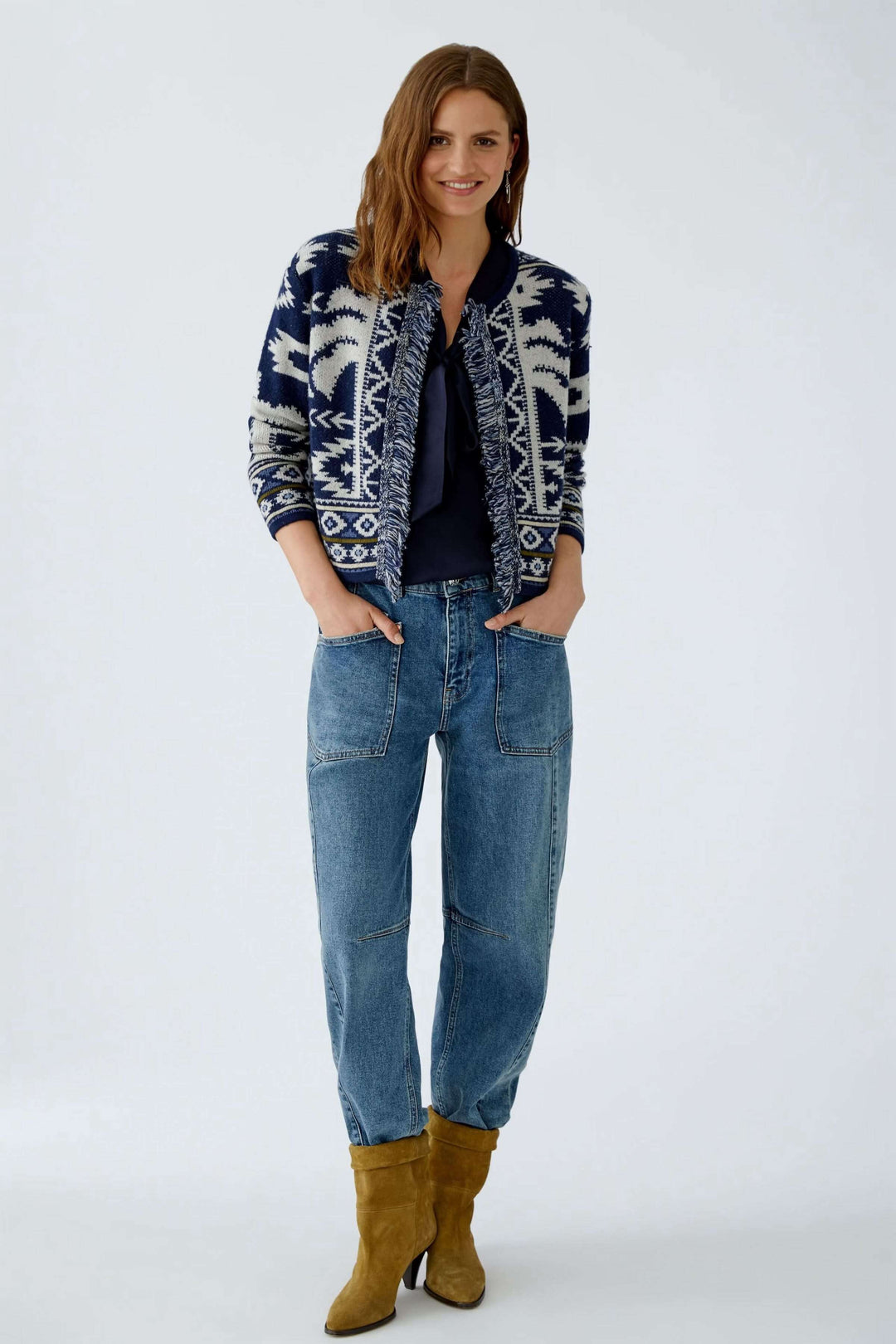 Femme portant un cardigan motif western en jacquard avec franges, jeans décontractés et bottes en cuir.