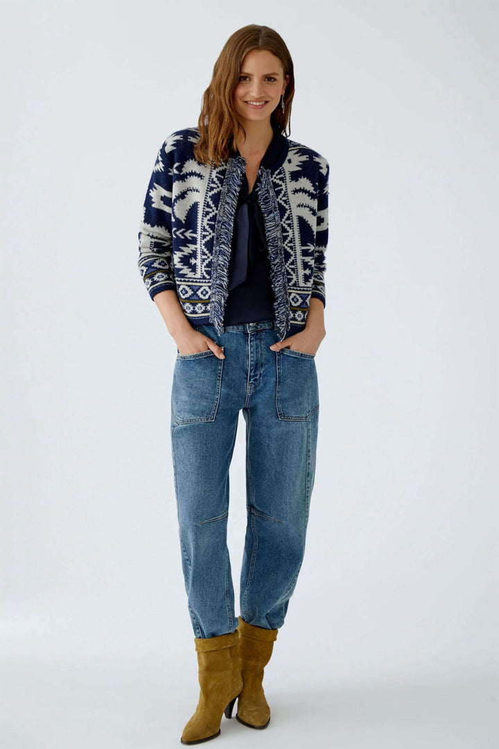 Femme portant un cardigan motif western en jacquard avec franges, jeans décontractés et bottes en cuir.