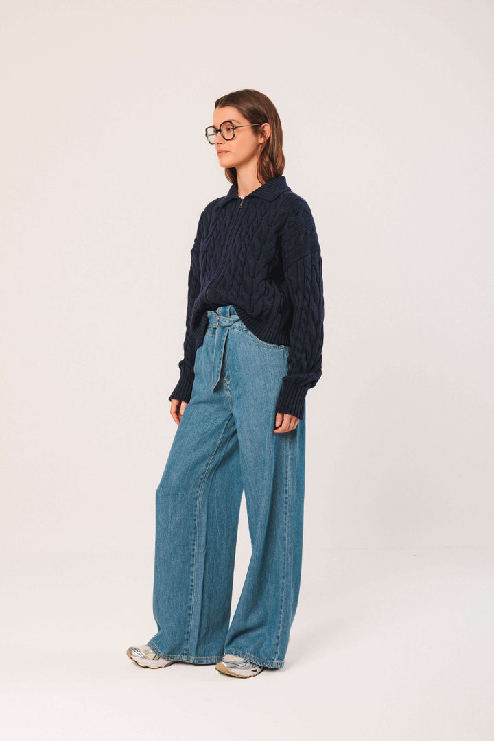 Femme portant un cardigan à torsades bleu marine avec un jean large, style moderne et décontracté.