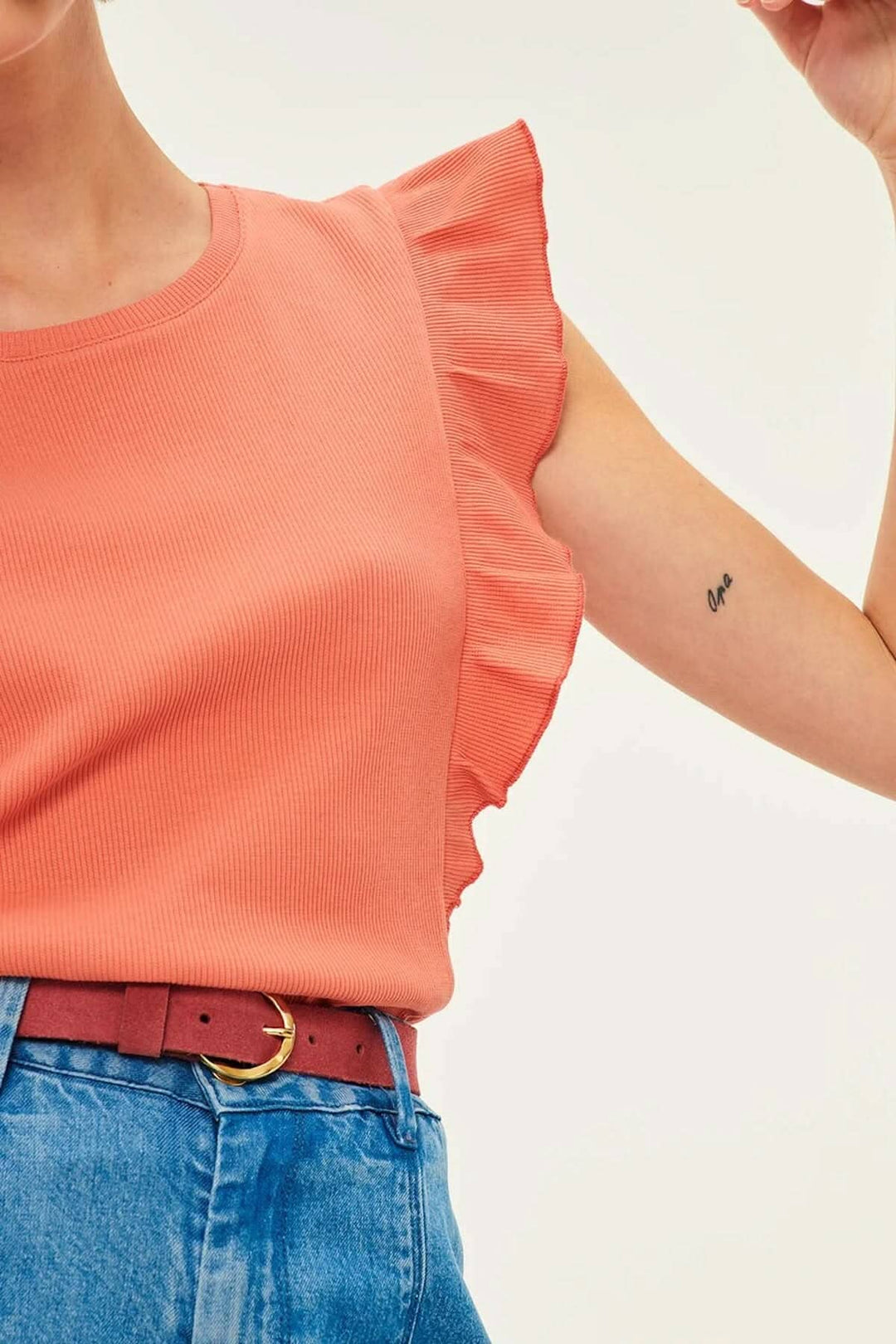 Femme portant un top corail à volants et une ceinture marron avec boucle dorée, style bohème chic.
