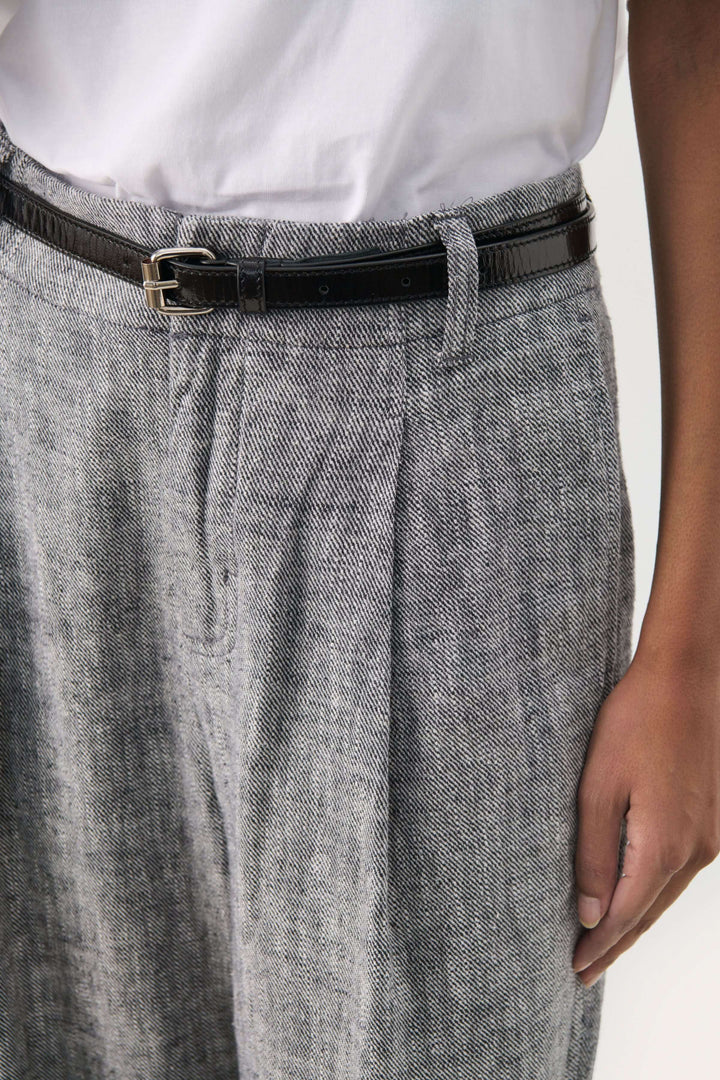 Ceinture noire en cuir sur pantalon à plis, ajoutant une touche élégante à la tenue.