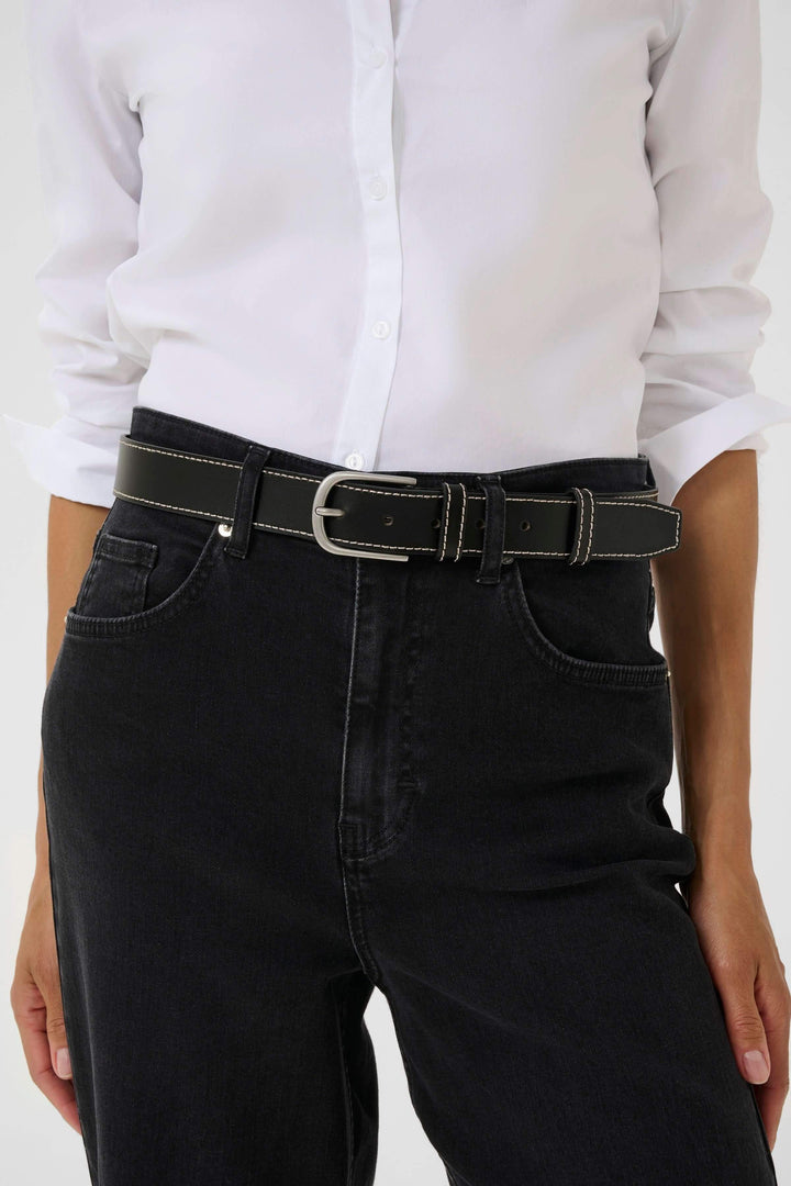 Ceinture Seyra en cuir noir avec surpiqûres contrastantes, portée sur un pantalon noir avec une chemise blanche.