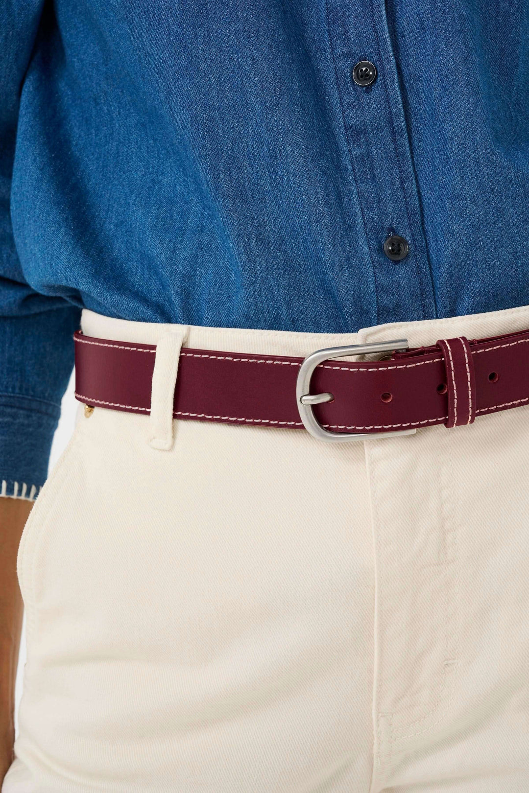 Ceinture en cuir bordeaux avec boucle classique, portée sur pantalon beige, ajoutant une touche élégante à la tenue.