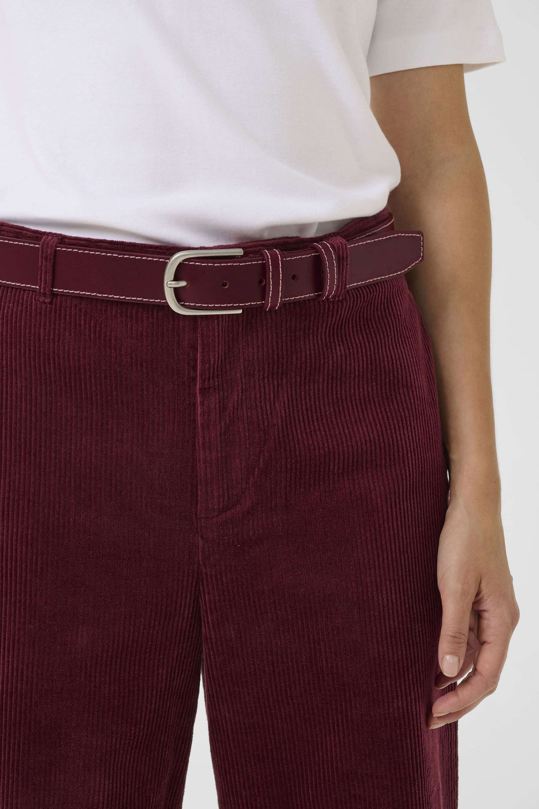 Ceinture Seyra en cuir bordeaux avec boucle métallique, portée avec un pantalon en velours côtelé. Accessoire chic.