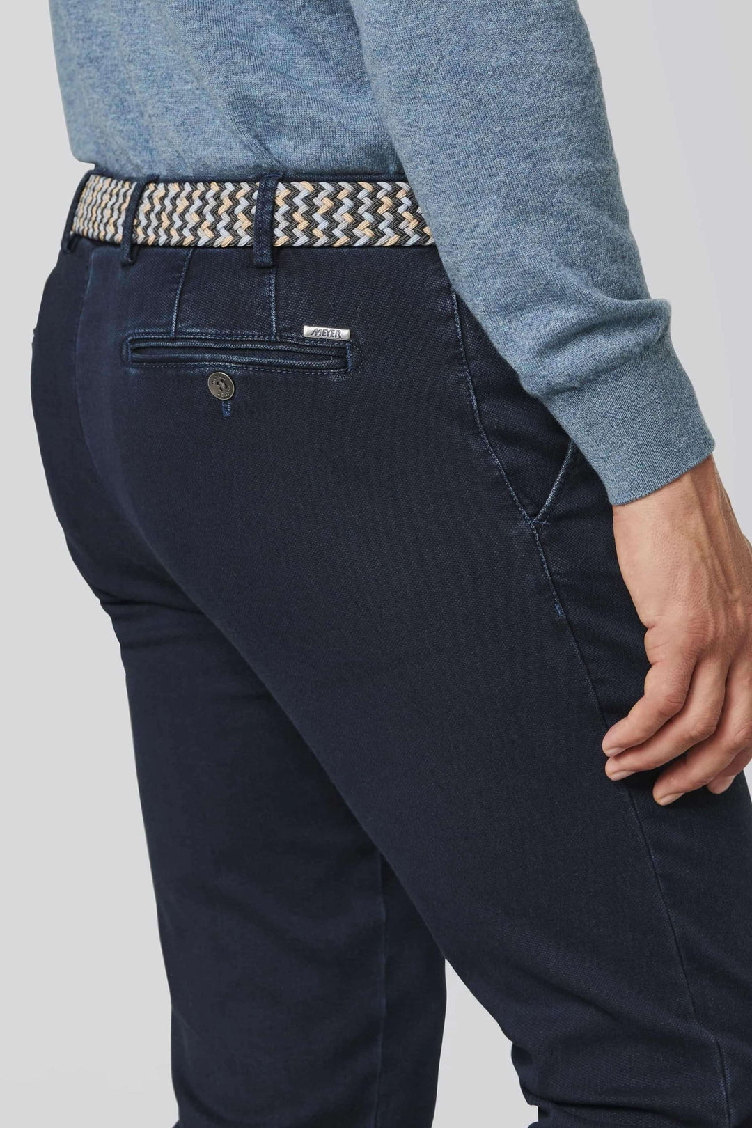 Ceinture tressée multicolore portée avec un pantalon bleu, ajoutant texture et style décontracté.
