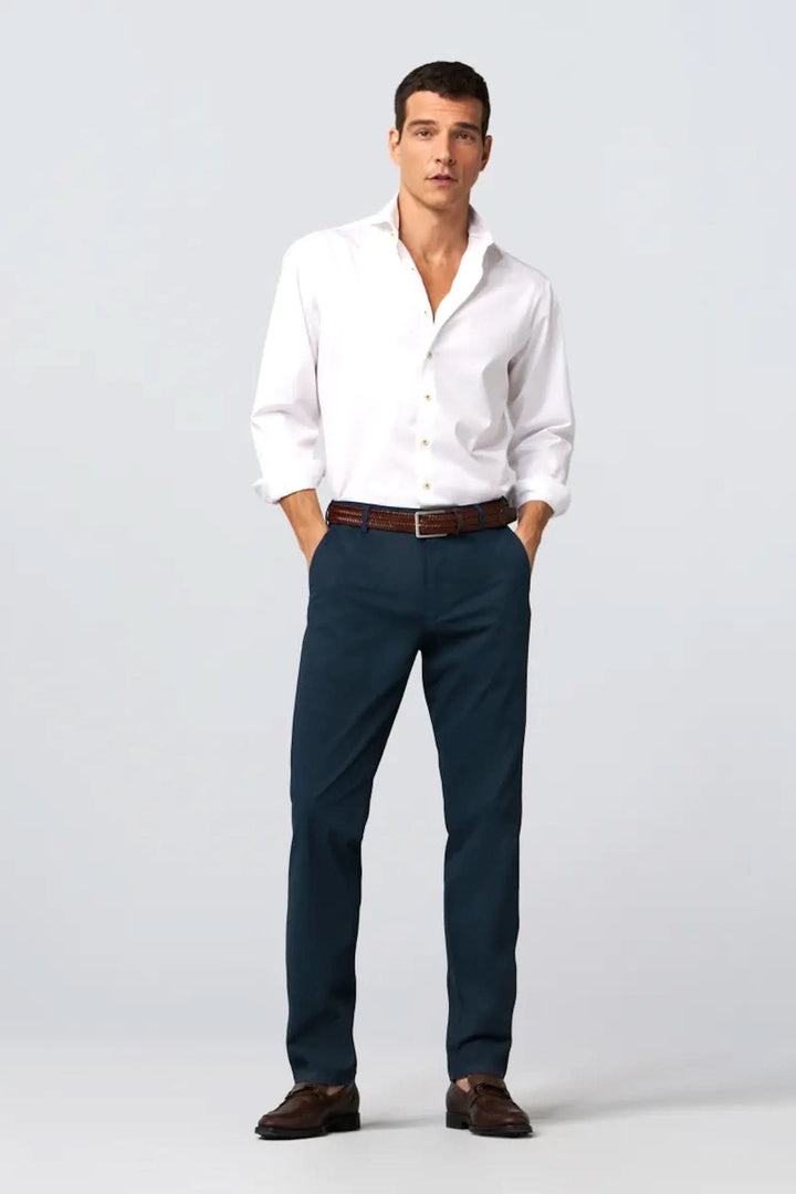 Homme portant une chemise blanche avec un pantalon bleu et une ceinture tressée en cuir, style décontracté.