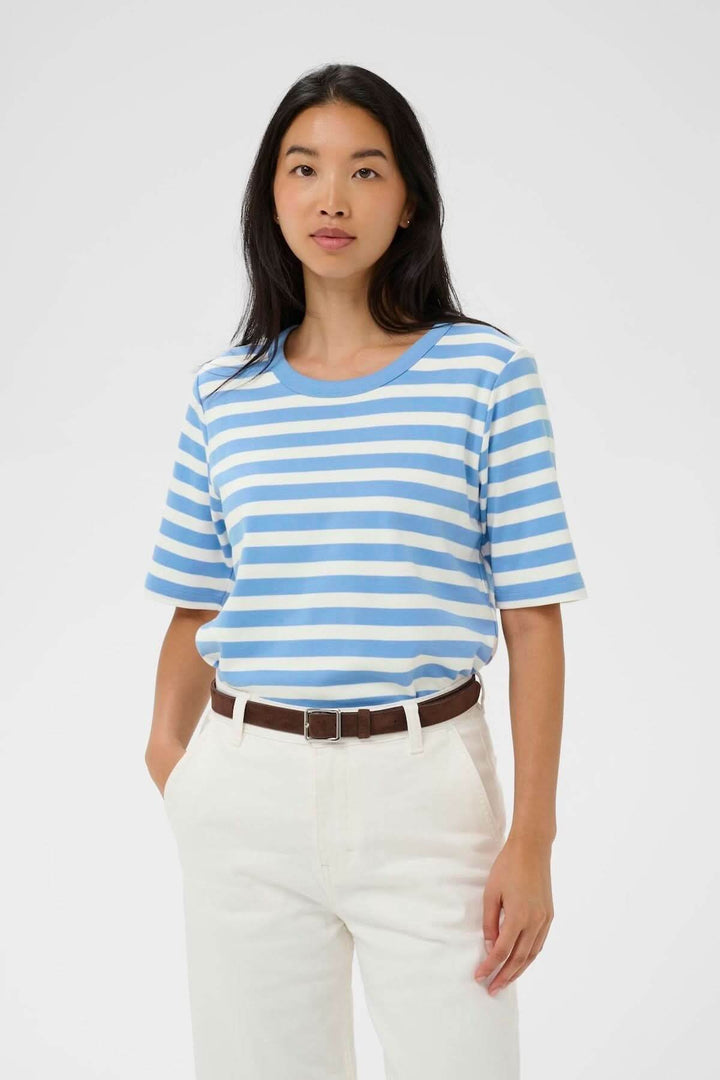 Femme portant le Chandail Ratana ligné, haut à rayures bleues et blanches, coupe droite et encolure arrondie, style décontracté.