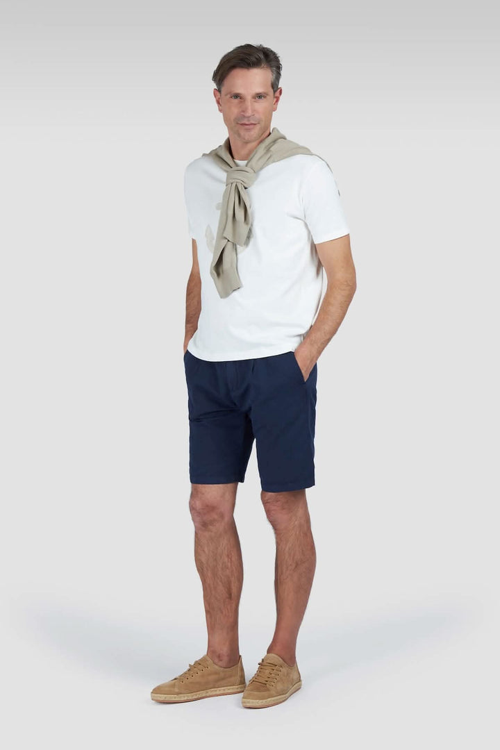Homme en t-shirt blanc et short navy avec un pull autour du cou, look décontracté et élégant.