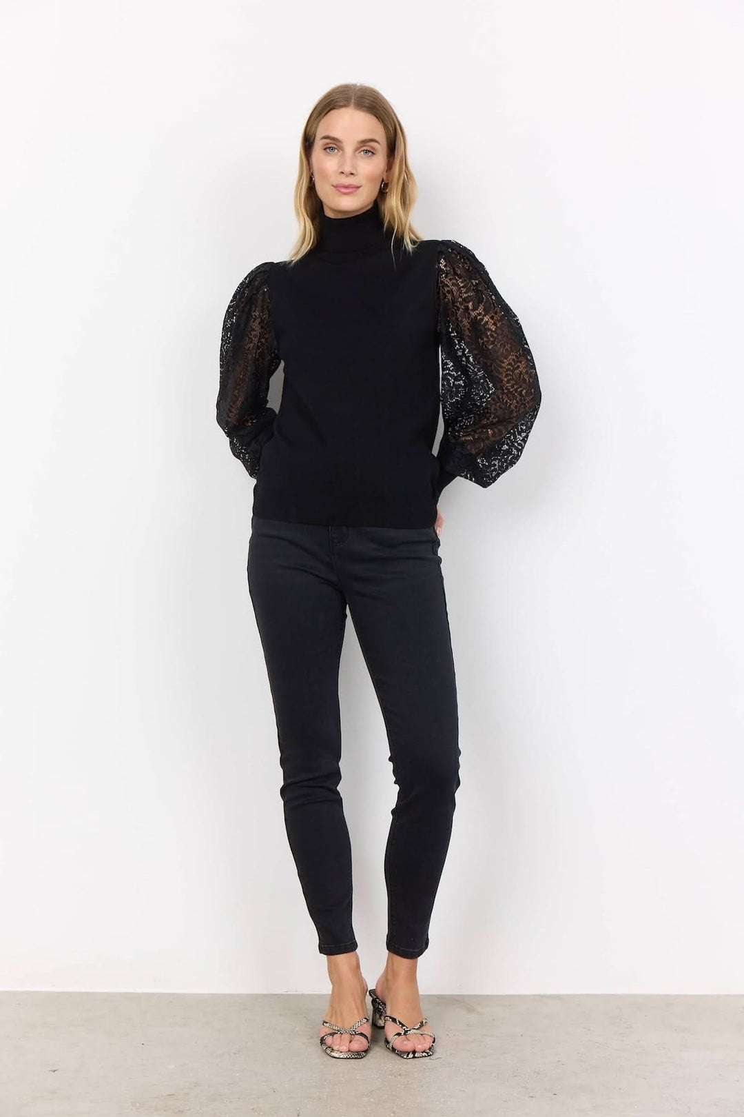 Chandail à col montant noir avec manches en dentelle transparente pour un style chic et féminin.