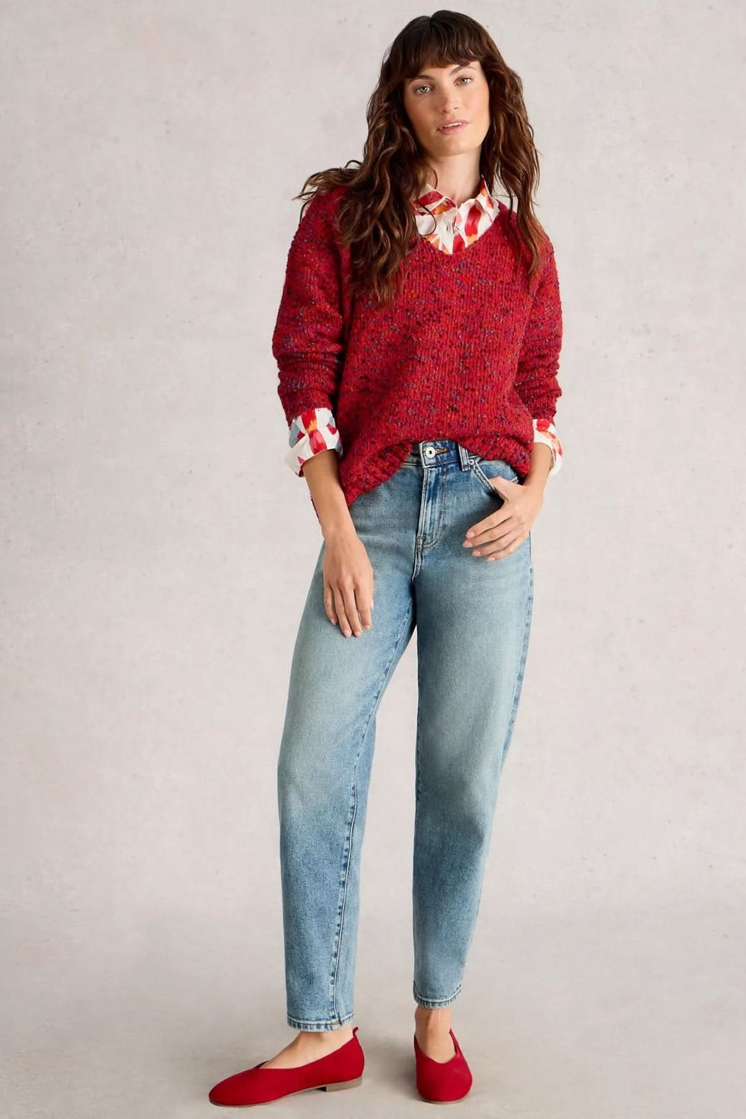 Chandail col en V rouge associé à une chemise à motifs et un jean décontracté, look moderne et confortable.