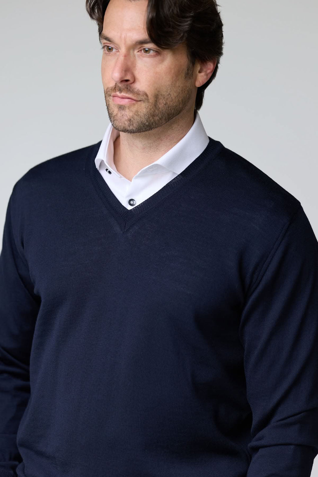 Homme portant un chandail col en V en laine mérinos marine avec chemise blanche pour un style élégant et intemporel.