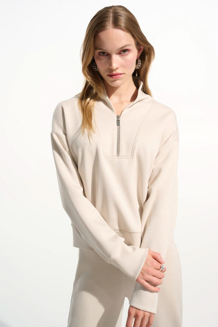 Femme portant un chandail à col montant beige avec demi-zip, manches longues et coupe décontractée, style moderne et élégant.