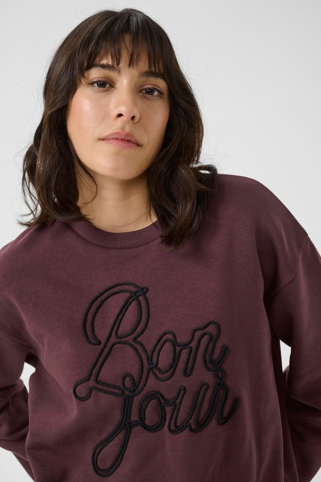 Chandail à col rond bordeaux avec inscription brodée 'Bonjour', style universitaire décontracté pour une allure moderne.