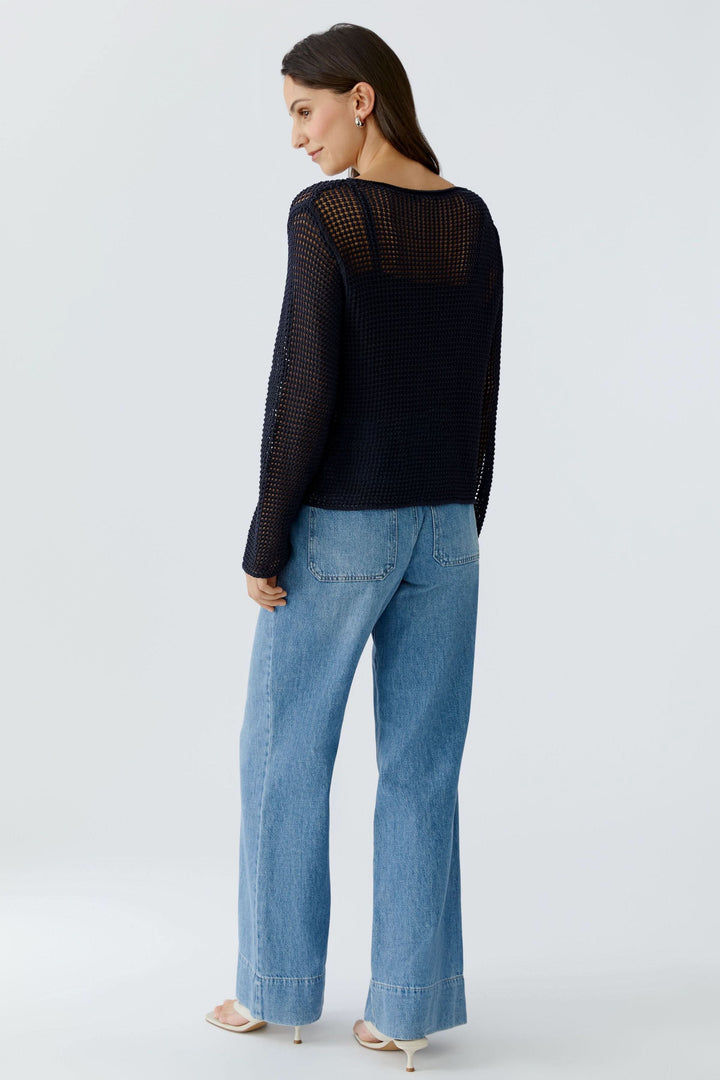 Femme portant un chandail en maille ajourée à manches longues, vue arrière, avec un jean, sur fond neutre.