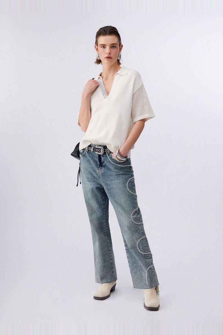 Chandail en maille avec col polo et strass, manches courtes et inserts ajourés, porté avec un jean et bottes blanches.