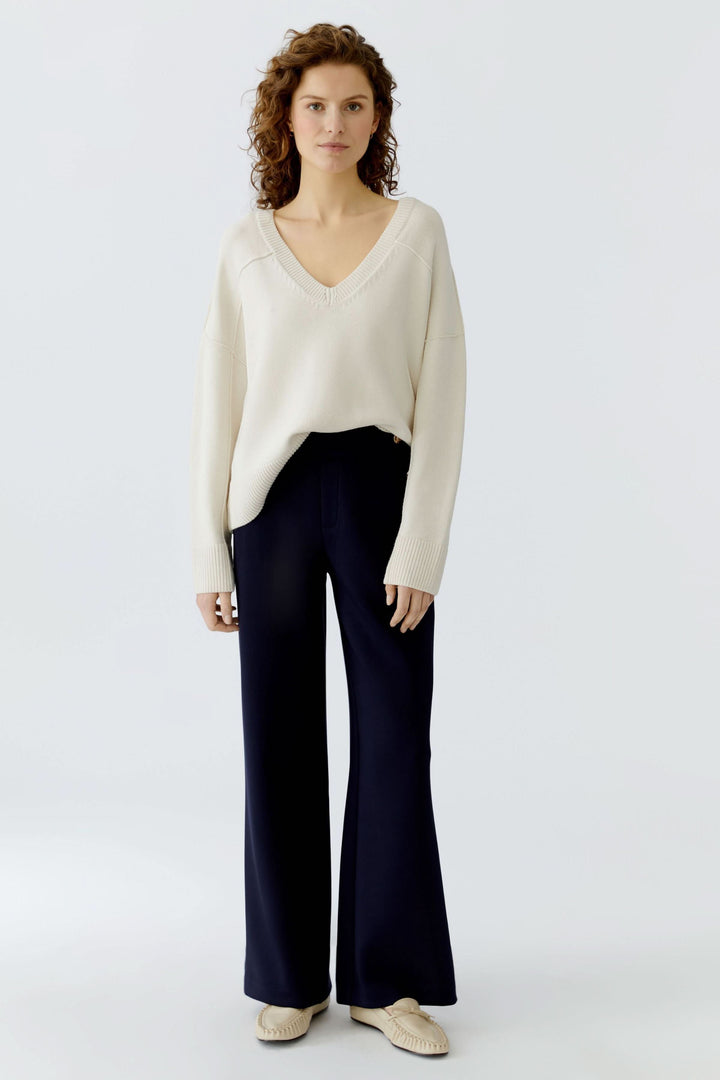Chandail en maille à col en V blanc porté avec un pantalon bleu, style épuré et intemporel.