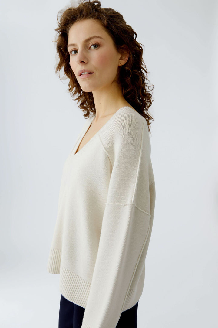 Chandail en maille à col en V porté par une femme, style épuré, manches longues, coupe ample, couleur crème, décontracté et élégant.