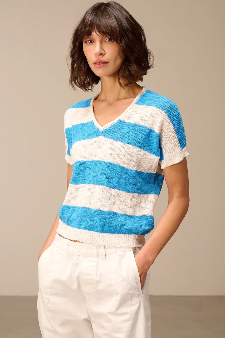 Femme portant un chandail en maille à col en V avec rayures bleues et blanches, manches courtes, moderne et estival.