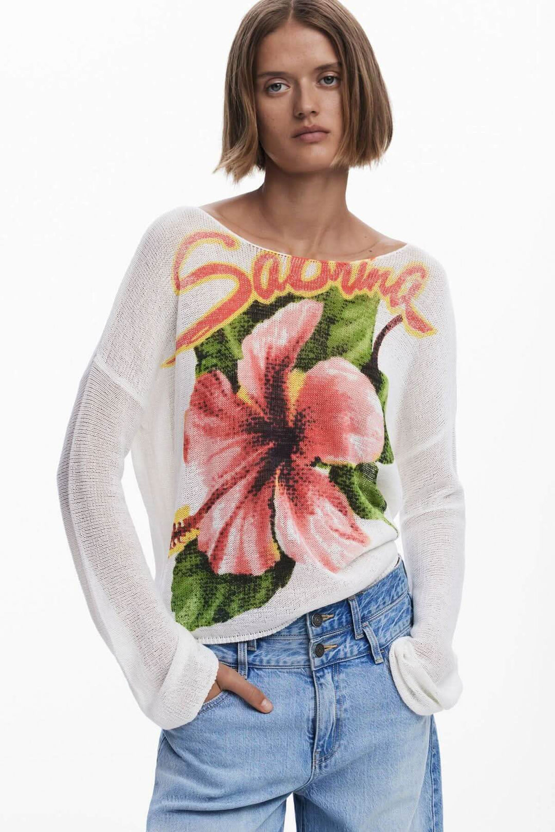 Chandail en maille fine avec imprimé floral coloré et encolure bateau, porté avec un jean décontracté.