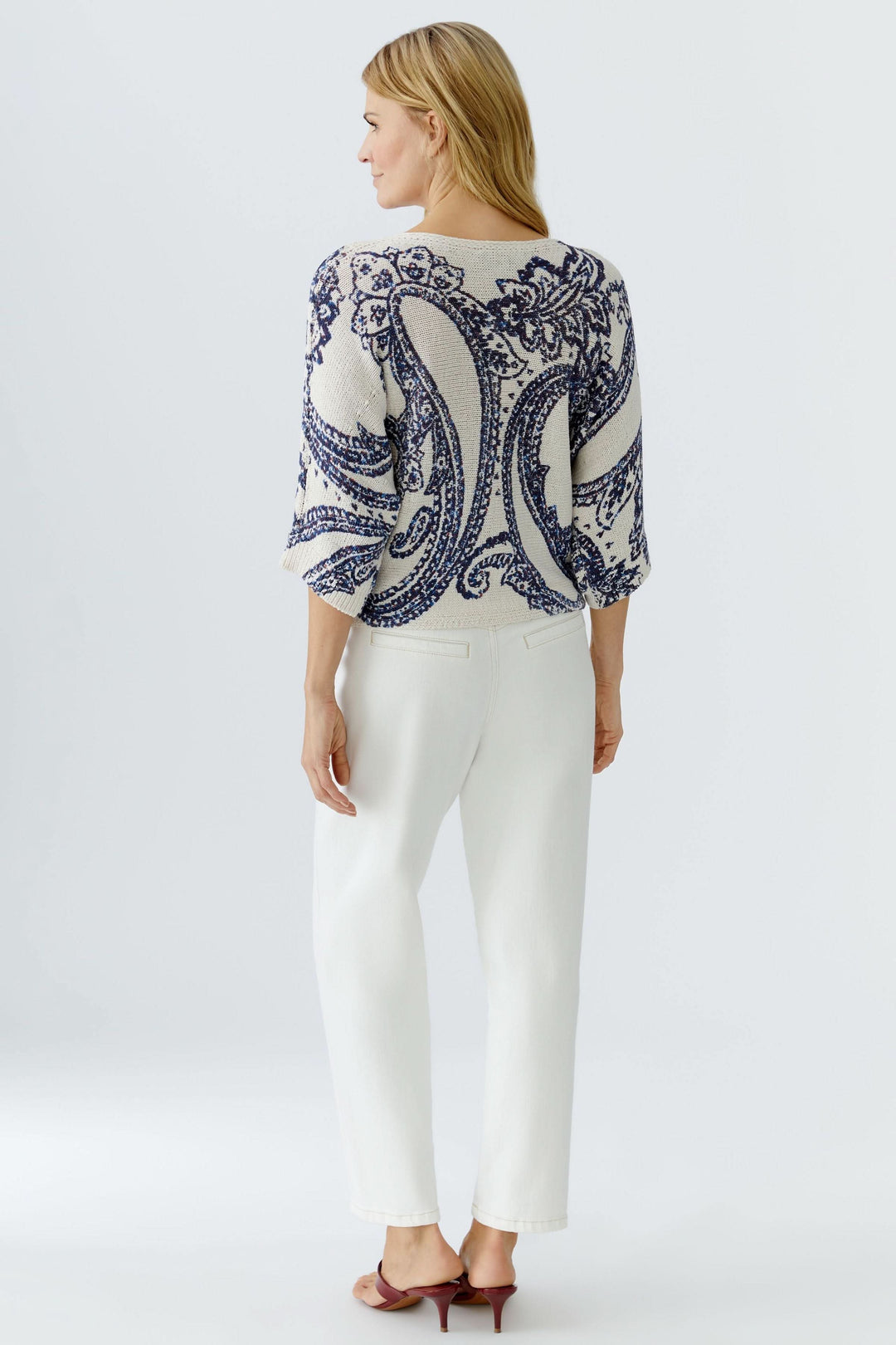 Femme portant un chandail en maille à motif cachemire, manches trois-quarts, sur un fond blanc, créant une allure chic et moderne.