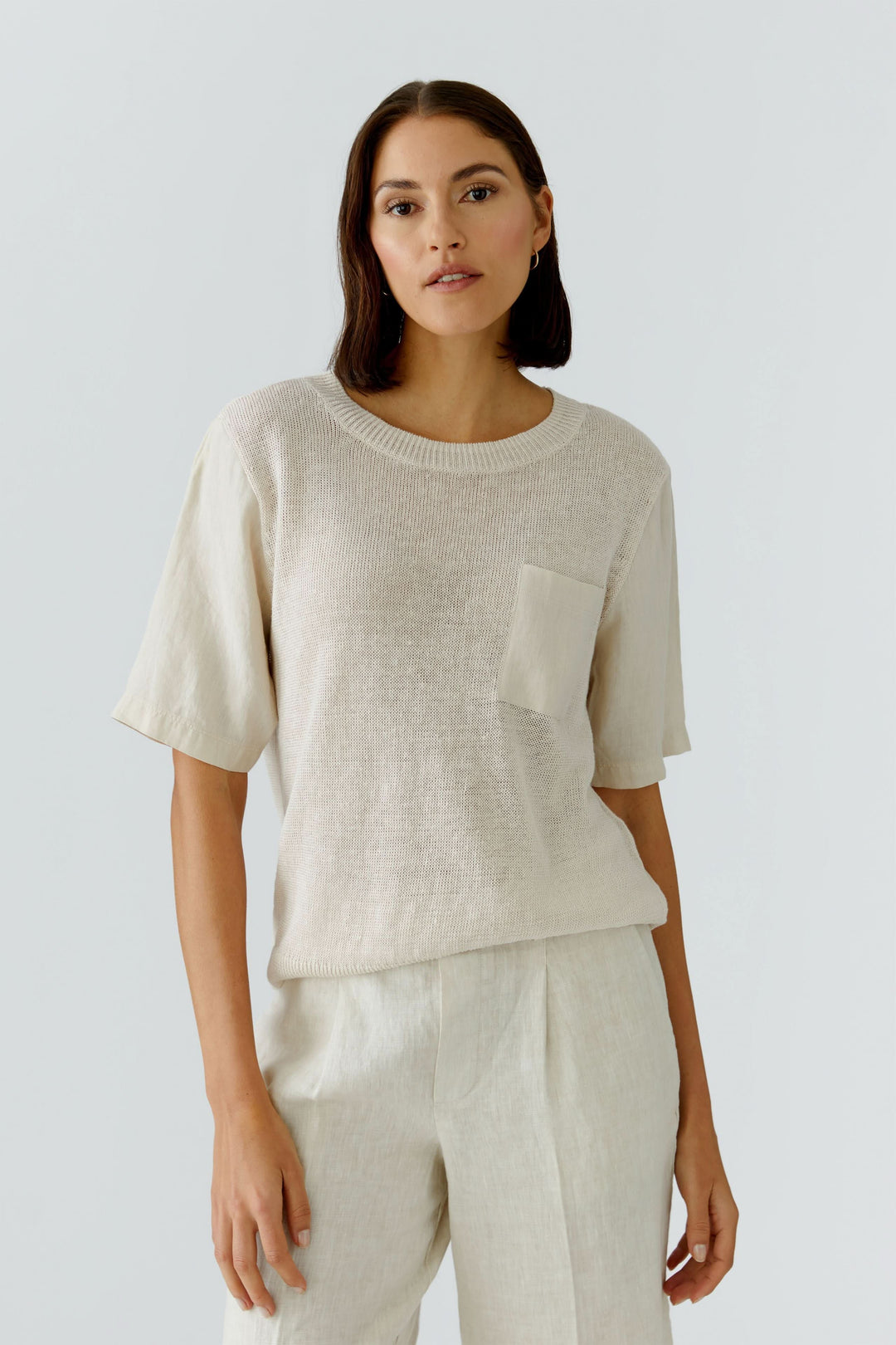 Femme portant un chandail en maille texturée à manches courtes avec poche poitrine, design moderne pour un style naturel.