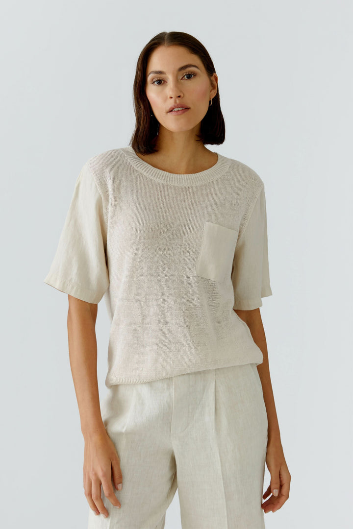 Femme portant un chandail en maille texturée à manches courtes avec poche poitrine, design moderne pour un style naturel.