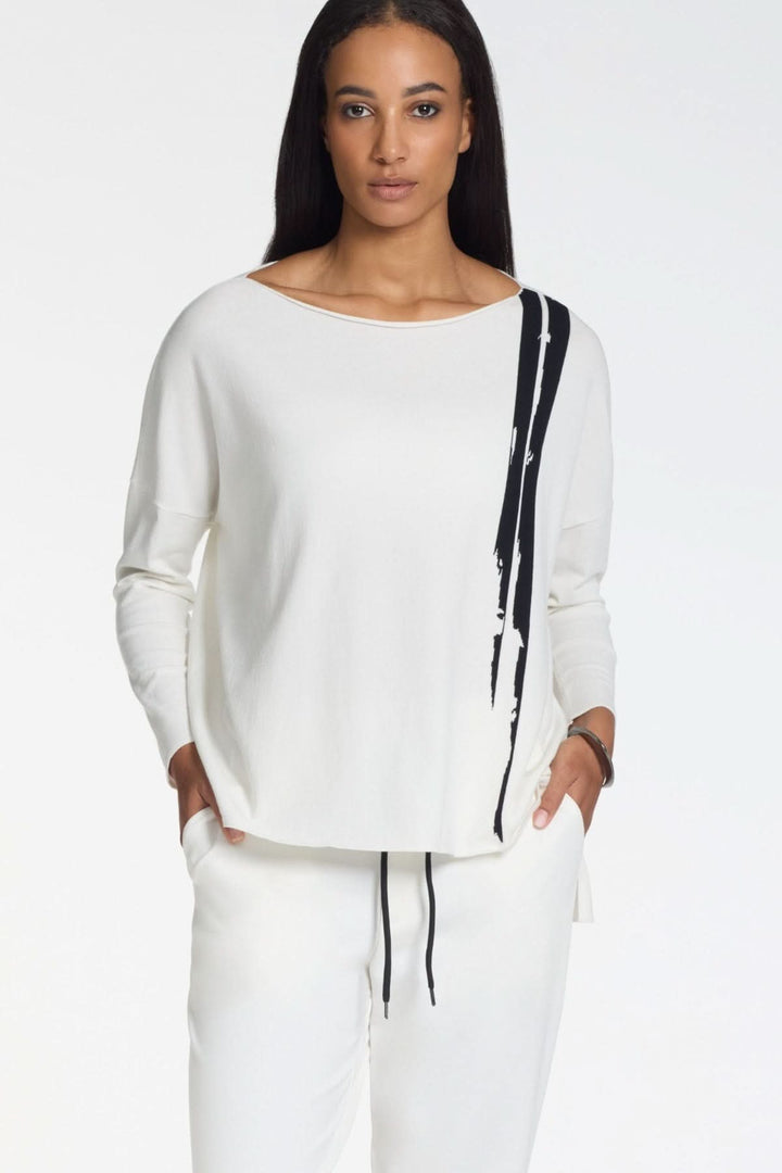 Femme portant un chandail fluide à motif graphique manches longues blanc avec encolure bateau.