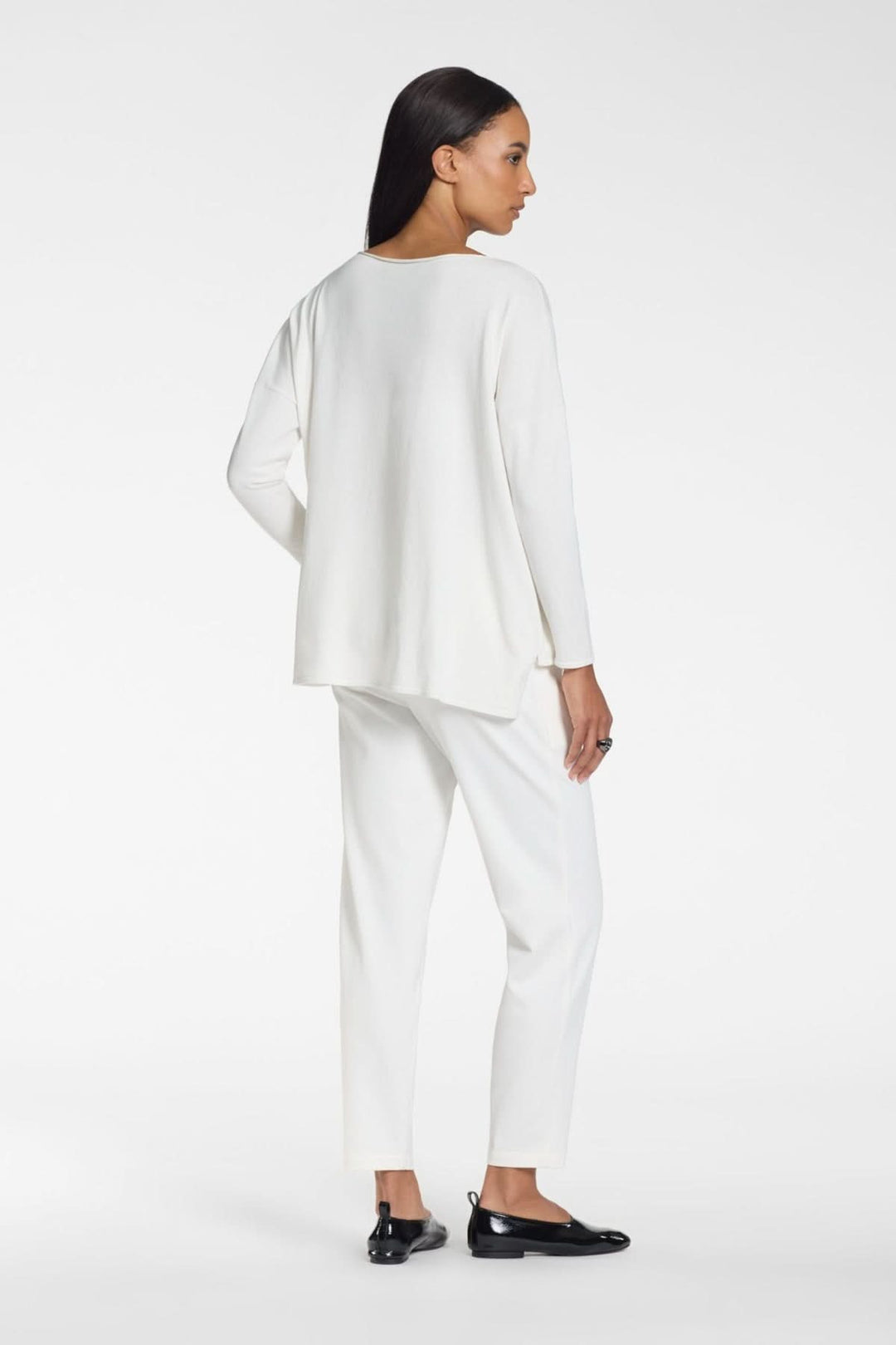 Femme portant un ensemble blanc, vue de dos, style épuré avec pantalon et haut manches longues, allure moderne et minimaliste.