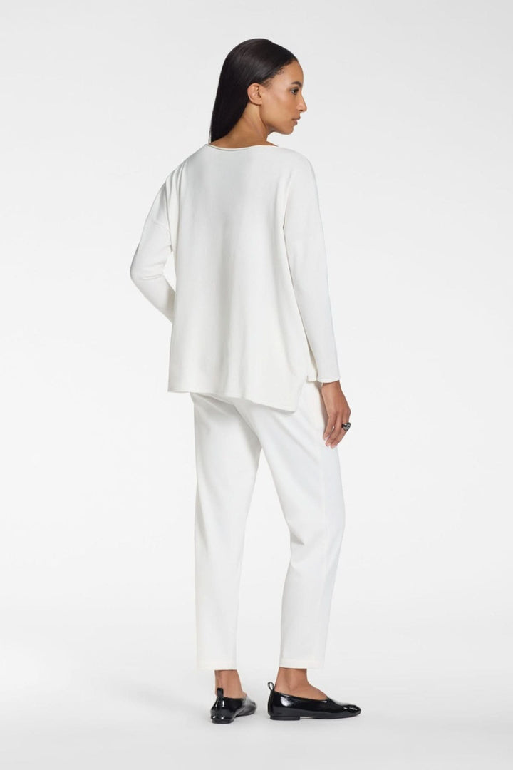 Femme portant un ensemble blanc, vue de dos, style épuré avec pantalon et haut manches longues, allure moderne et minimaliste.