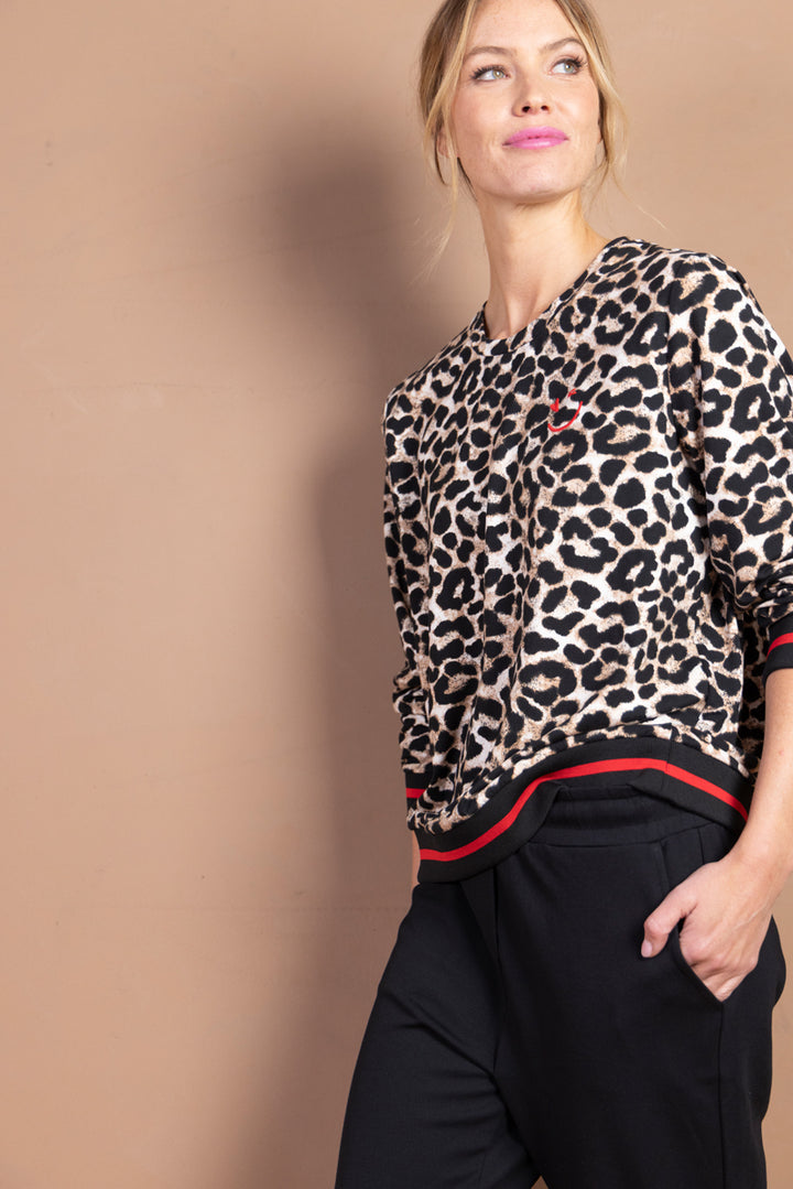 Femme portant un chandail imprimé léopard avec finitions sport chic, style polyvalent pour look moderne et affirmé.