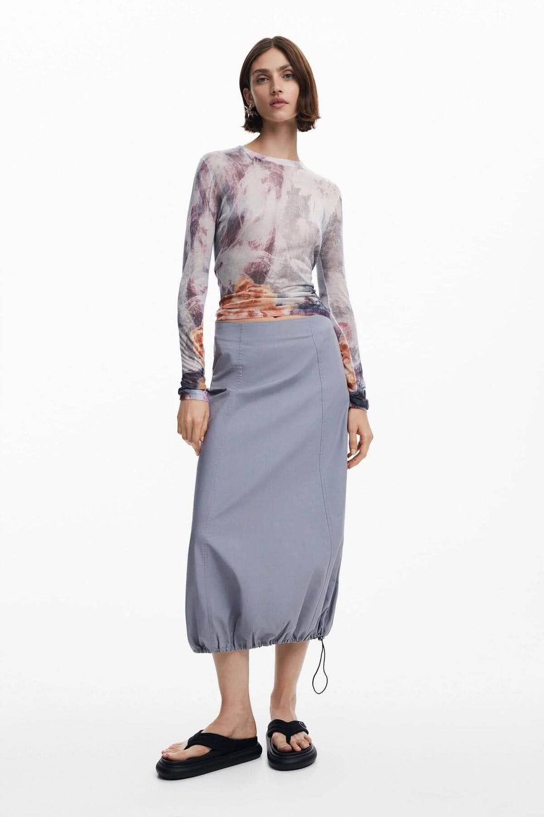 Femme portant un chandail imprimés flous avec col montant et jupe grise, look moderne et chic.