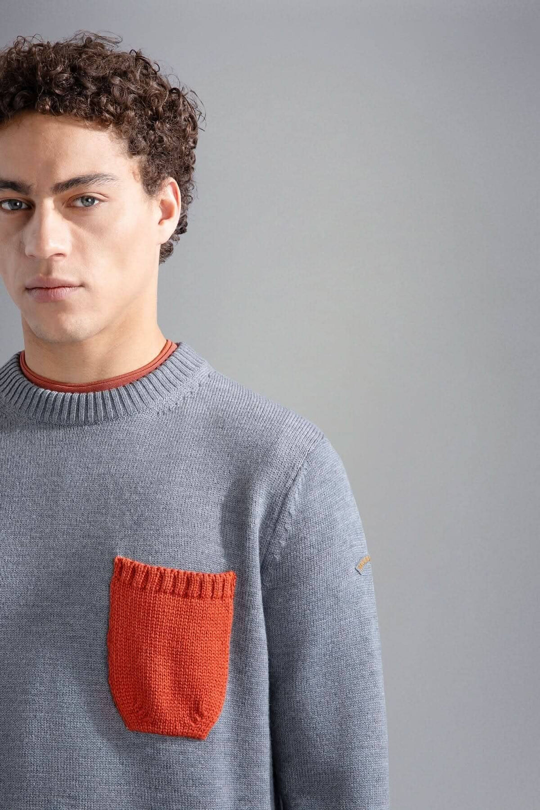Pull gris clair avec poche contrastante orange, col rond classique, look décontracté et stylé.