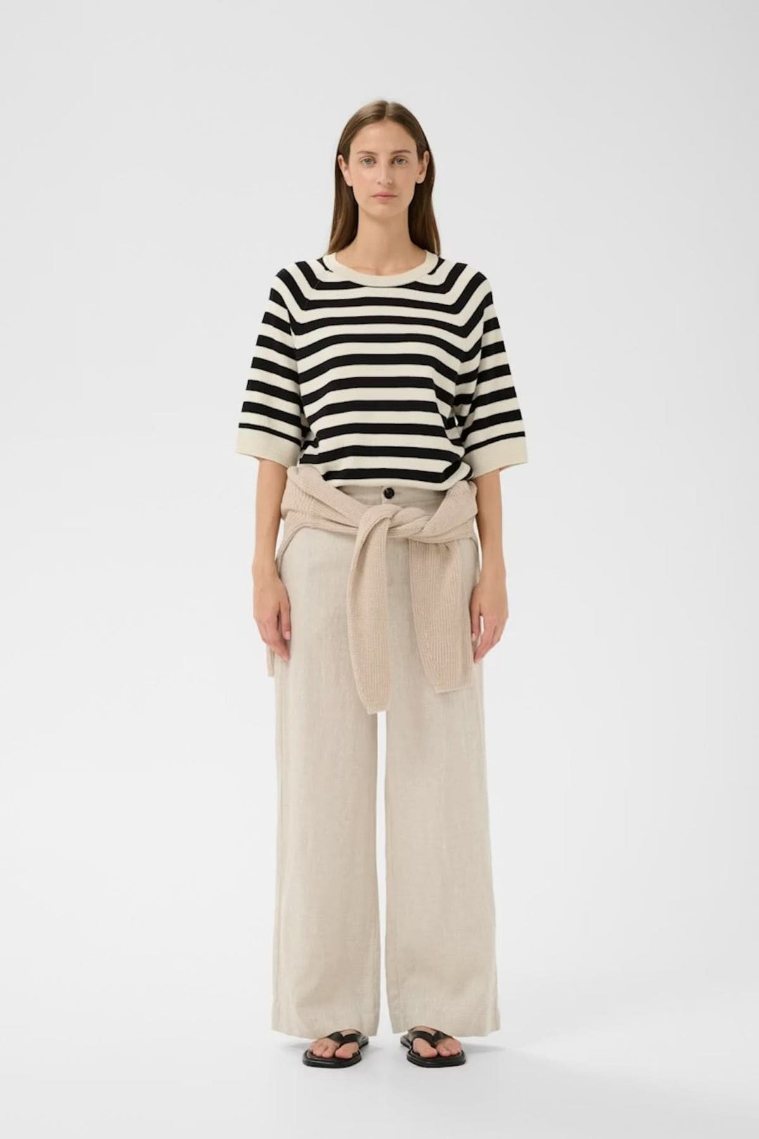 Chandail rayé en tricot Madie à rayures noires et blanches, coupe droite, encolure ronde, porté avec un pantalon beige.