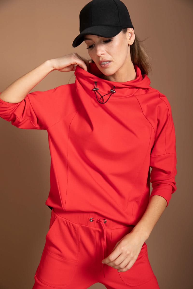 Modèle portant un chandail structuré rouge avec col montant et cordon ajustable, style athleisure confortable et moderne.