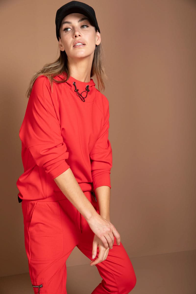 Femme portant un chandail structuré rouge avec col montant et cordon ajustable, tenue athleisure moderne.